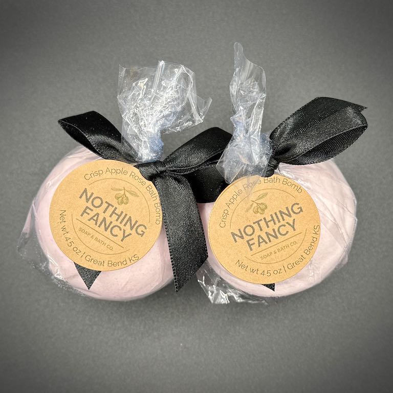 Two bath bombs with 'Nothing Fancy' labels and black ribbons on a gray background