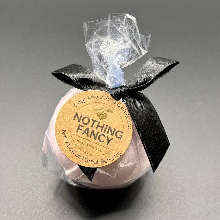 Bath bomb wrapped in clear plastic with a black ribbon and 'Nothing Fancy' label on a gray background