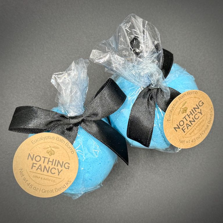 Two blue bath bombs with black ribbons and 'Nothing Fancy' labels on a gray background