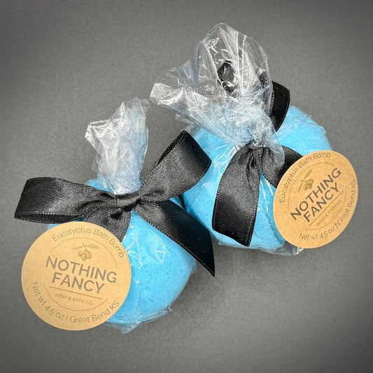 Two blue bath bombs with black ribbons and 'Nothing Fancy' labels on a gray background