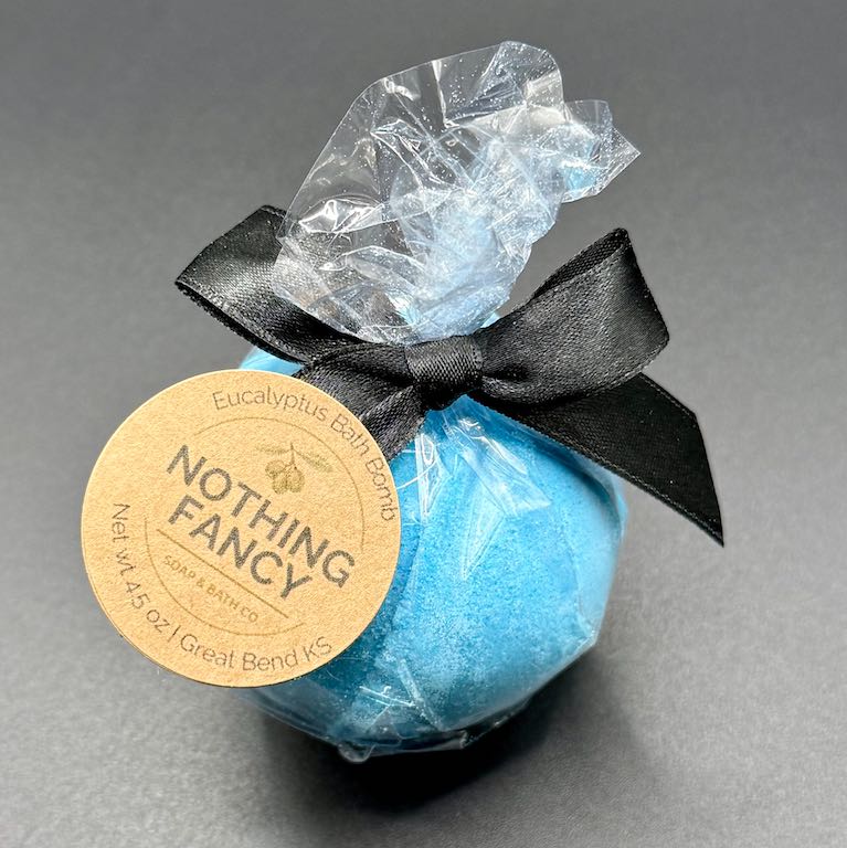 Blue bath bomb with a black ribbon and 'Nothing Fancy' label on a gray background
